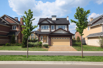 New two-storied brown brick cottage with garage in front of it.