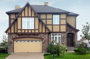 New two-storied brown stone cottage with beige garage and roof.