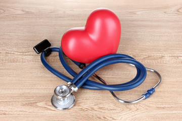 Medical stethoscope and heart on wooden background