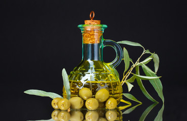 olive oil in jar and olives on black background