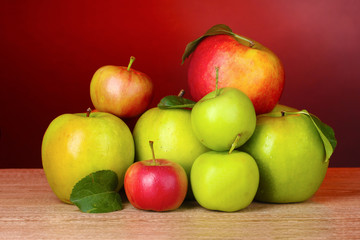 Many fresh organic apples on wooden table on red background