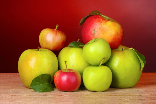 Many fresh organic apples on wooden table on red background