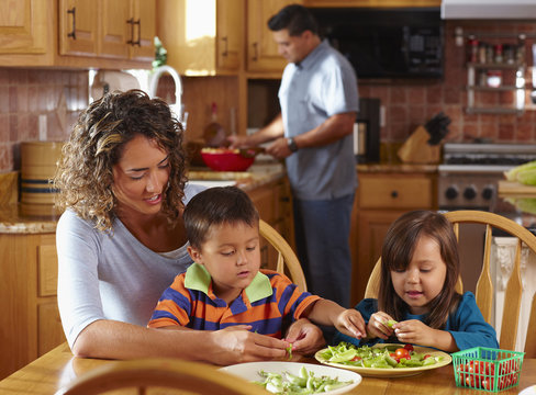 "Mother, son and daughter shelling peas at dining table"