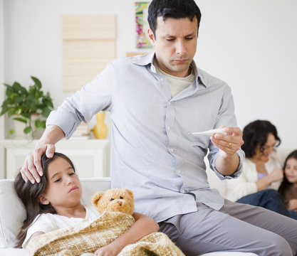 Father taking sick daughter&rsquo;s temperature with thermometer