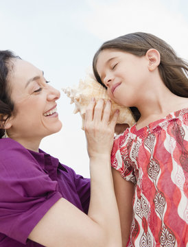 Mother holding seashell to daughter&rsquo;s ear