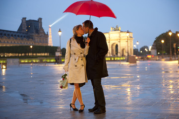 Caucasian couple kissing in rain at night near the Louvre