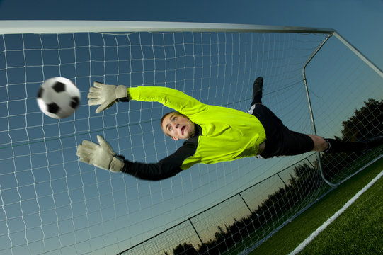 Caucasian goalie deflecting soccer ball