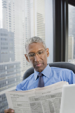 Mixed race businessman reading newspaper at desk