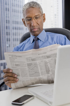 Mixed race businessman reading newspaper at desk