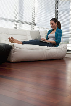 Hispanic woman on sofa using laptop