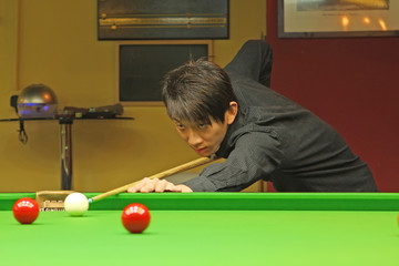 Young man concentrating while aiming at pool ball while playing