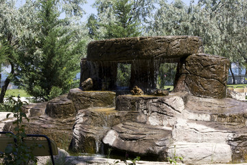 waterfall ove structure of stones in a park in front of trees
