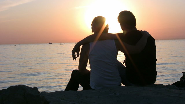 Couple sitting at the beach during sunset