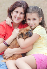 Latin girl and  her mother hugging the family dog
