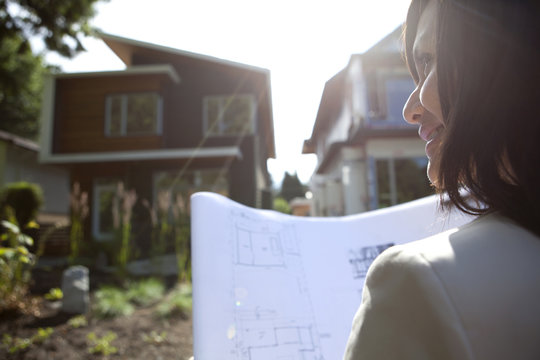 Mixed race real estate agent standing near house reviewing blueprints