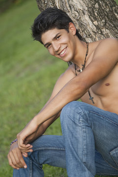 Bare chested Hispanic man leaning against tree