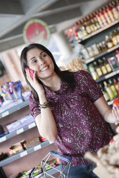 Hispanic woman talking on cell phone and shopping in grocery store
