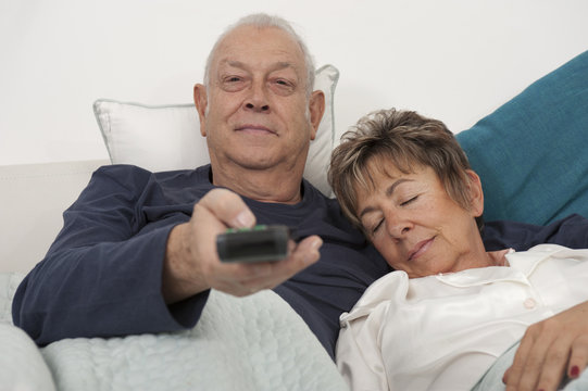 Senior Hispanic couple laying in bed watching television