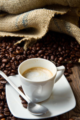 Coffee cup with burlap sack of roasted beans on rustic table