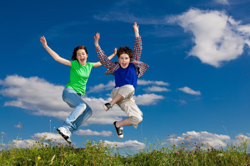 Girl and boy jumping against blue sky