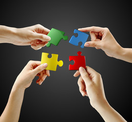 Hands and puzzle on black background. Teamwork solving a puzzle
