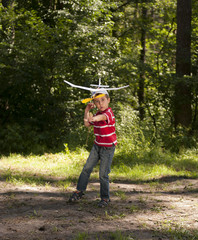 Boy launching toy airplane in summer forest