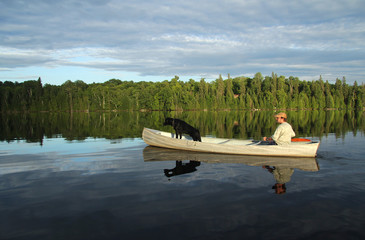 Man Paddling a Canoe with a Black Labrador Retriever in the Bow - Ontario, Canada