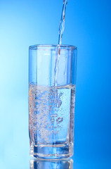 Pouring water on glass on blue background