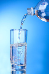 Pouring water on glass on blue background