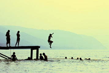silhouettes of children jumping off the dock - obrazy, fototapety, plakaty