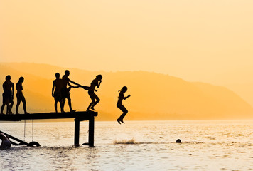 kids jumping off dock at sunset - obrazy, fototapety, plakaty