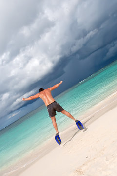 Tanned man jump in blue flippers on sand beach and ocean
