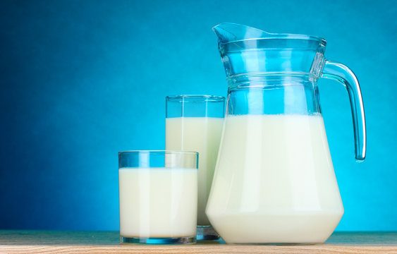 Tasty milk in jug and glasses on blue background
