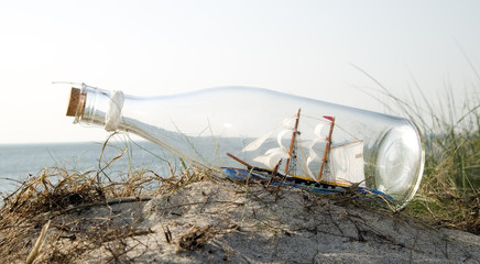 Miniature ship in bottle standing on sand