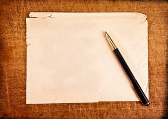 Ink pen and an old torn envelope on a wooden background.
