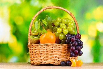 Ripe juicy fruits in basket on wooden table on green background