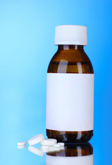 Liquid medicine in glass bottle and pills on blue background