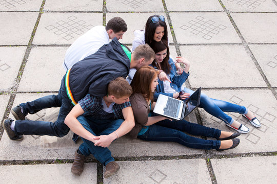 Group of male and female students sitting with a laptop on stree