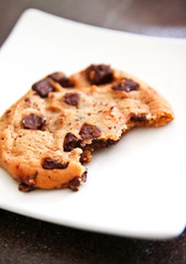 One chocolate chip cookie with a bite on dish