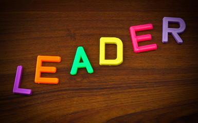 Leader in colorful toy letters on wood background