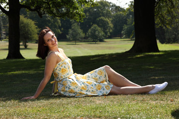 Naklejka na ściany i meble Happy young woman tanning in park summer sunshine