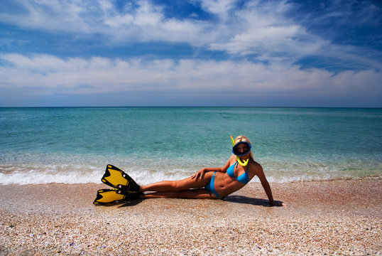 Blonde girl in yellow flippers and swimming mask on the sandy se