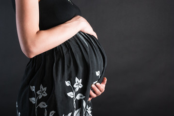 Stomach of the pregnant woman in a dark dress with white colors