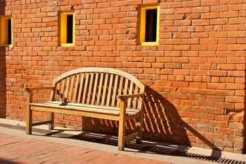Wooden Bench Sitting by Orange Brick Wall with Yellow Windows