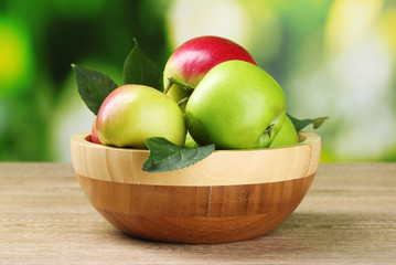 Fresh organic apples in plate on wooden table outside