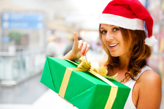 Young smiling woman holding gift standing at shopping mall weari