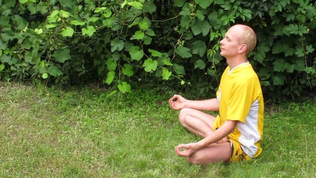 Man in yellow in meditation. On grass.