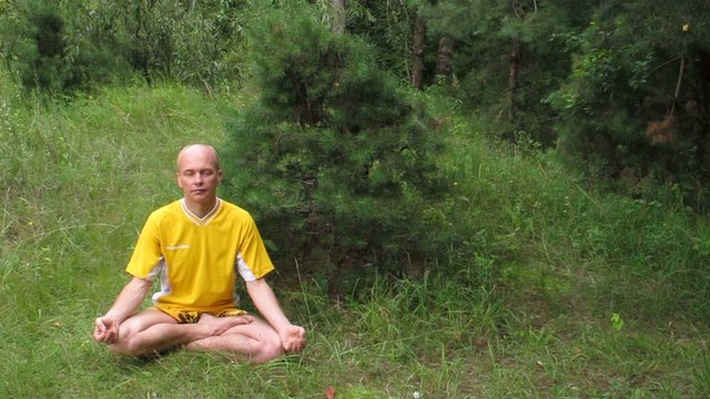 Man in yellow in meditation. On green grass.