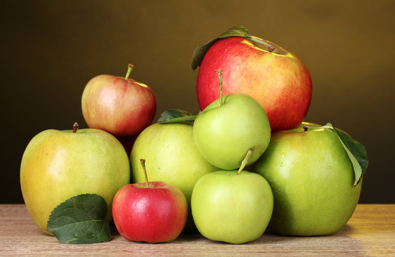 Many fresh organic apples on wooden table on yellow background