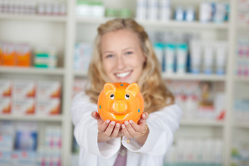 blonde lächelnde apothekerin zeigt sparschwein